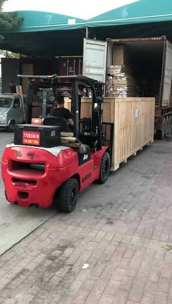 Warehouse staff loading a wooden crate into a shipping container by forklift